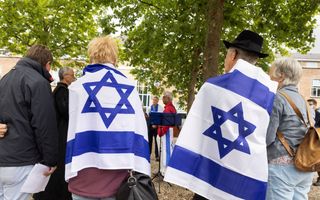 Vier mensen staan op een rij, op de rug gefotografeerd. Twee van hen hebben een Israëlische vlag omgeslagen.