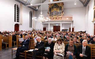 Oude dorpskerk vol mensen, die A-viertjes voor zich hebben en zingen.