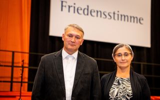 Echtpaar uit Kazachstan, breedgeschouderde man met grijzend haar in een scheiding opzij, vrouw met grijzend haar met een hoofddoekje erop, donkere ogen, bril, donkere kleren aan 