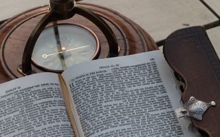 Opengeslagen Bijbel ligt bovenop kompas.