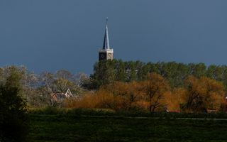 Kerktoren steekt uit boven herfstbomen.