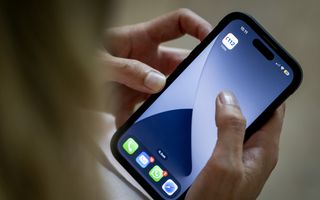 Twee blanke handen houden smartphone vast, duim en wijsvinger goed zichtbaar. Boven in het scherm staat een 112-appicoon. 