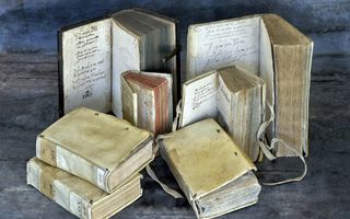 Opgestapelde en opengeslagen oude boeken, met perkamenten bandjes en (aan de binnenkant) handgeschreven aantekeningen.