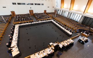 Luchtfoto van vergadertafels in een modern kerkgebouw met zo’n veertig mannen daaraan.