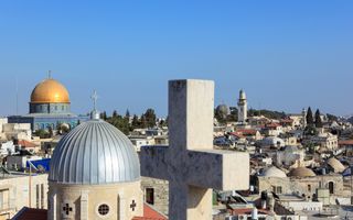 Zicht op Jeruzalem. Op de voorgrond een groot kruis en een koepeltoren. Op de achtergrond een gouden koepel en een kerktoren.