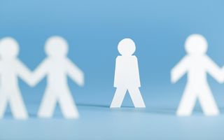 Uit wit papier geknipte poppetjes, aan elkaar verbonden via de handen. In het midden onderbreekt een poppetje de rij door met de armen strak langs het lijf te gaan staan. 