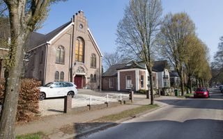 Bakstenen kerkgebouw langs een weg met bomen.