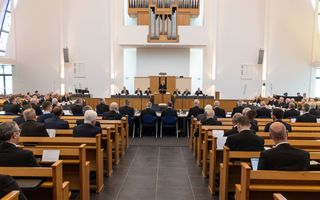 In een modern kerkgebouw vergaderen mannen in zwarte pakken.