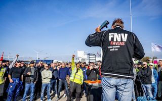 Mannen staan te luisteren naar een man met achterop zijn jasje de tekst: ”FNV havens, sterke vakbond = goede cao”