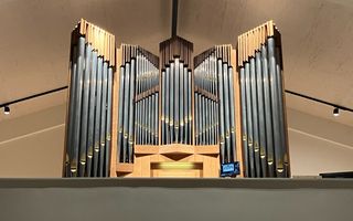 Een orgelfront in een nieuwe kerk met naast de speeltafel een beeldscherm.