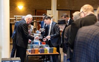 Mensen staan rond een tafel met boeken erop.