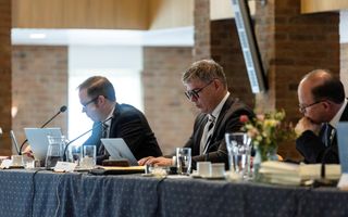 Man met bril achter een laptop. Aan weerszijden van hem twee andere mannen.