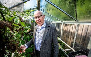 Een man met een colbert aan en een bril op staat in een kas met een paar vruchten in zijn hand.
