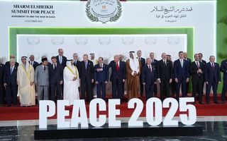 Mannen in donker pak en traditionele Arabische gewaden poseren voor groepsfoto op podium.