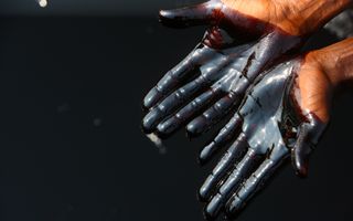 Een paar handen tegen een donkere achtergrond. Op de handen zit dikke olie.