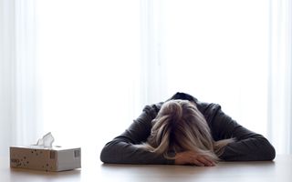 Vrouw ligt voorover op een tafel met haar hoofd op haar armen.