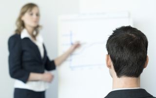 Een man met donker haar kijkt naar een vrouw die een presentatie geeft.