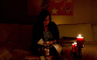 Een vrouw op een bank leest in het donker bij kaarslicht een tijdschrift.