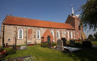Oud kerkgebouw met rode dakpannen; daarvoor een grasveld met grafstenen.
