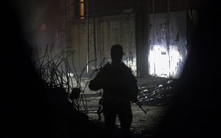 Man met geweer staat in donkere straat.