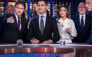 Vier mannen in pak en een vrouw achter een desk met glazen water.