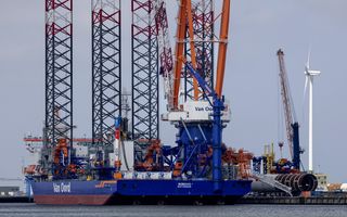Een groot blauw schip met kranen erop ligt in een haven. Op het schip staat in grote letters de naam van het bedrijf Van Oord.