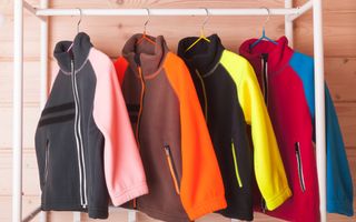 Felgekleurde fleecetruien aan hangers in een kast. 