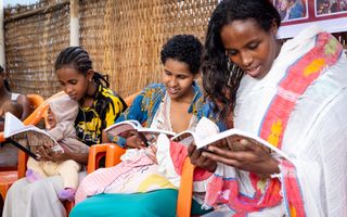 Jonge moeders, sommige met een kind op schoot, lezen in de Bijbel. 