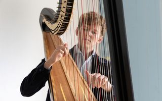 Harp met daarachter een jongeman met rossig haar en een zwart vest aan. Hij bespeelt de harp. 