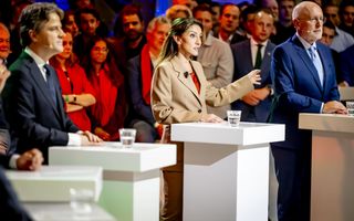 Drie lijsttrekkers, twee mannen en een vrouw, staan achter statafels met achter hen publiek. De middelste, Dilan Yeşilgöz, is aan het woord.