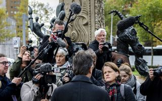 Journalisten met microfoons en camera’s praten met man in grijze jas.