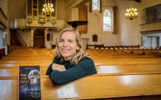Een jonge vrouw met halflang, blond haar zit op de achterste kerkbank. Op de achtergrond het interieur van de kerk. Op een van de kerkbanken ligt een kinderboek.