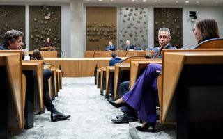 Twee mannen en een vrouw zitten in een Kamerzetel in de plenaire zaal van de Tweede Kamer.