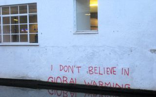 De leus „I don’t believe in global warming” op de muur van een wit gebouw, maar dan half onder water.