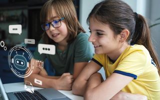 Twee kinderen, een jongen en een meisje, zijn enthousiast bezig met een gedeelde laptop waarop digitale chatbeelden te zien zijn. 