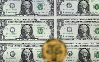 Een goudkleurige munt met een grote letter T tegen de achtergrond van bankbiljetten van 1 dollar.