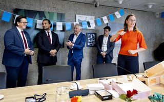 Vijf formeel geklede mensen achter een tafel waarop taart staat.