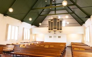 Kerkzaal met houten banken en een orgel.