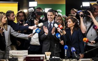 Rob Jetten, in het donker gekleed, wordt omringd door verslaggevers met microfoons.