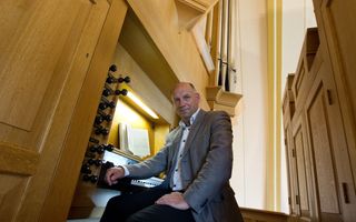 Een man in een grijs colbert kijkt in de camera. Een arm leunt op de klavieren van een kerkorgel.