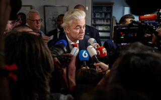 Man omringd door journalisten met microfoons en camera’s