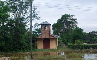 Een houten kerkje met een kruis op het dak; de weg ervoor is ondergelopen.