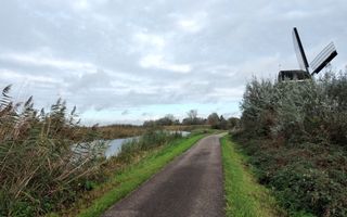 Asfaltpad dat leidt naar een molen. Links van het pad stroomt een vaart.