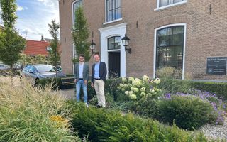Twee mannen staan in een tuin voor een voormalige pastorie