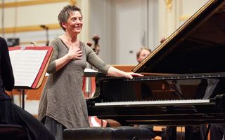 Een pianist staat op een podium naast een vleugel, met een hand op het instrument