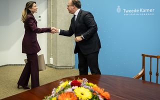 Man en vrouw, beiden in pak, schudden elkaar de hand. Op de voorgrond een tafel met een bloemstuk