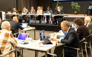 Mannen en vrouwen zitten aan tafels. Sommigen met een laptop of iPad voor zich.
