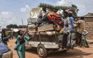 Mensen hangen aan de achterkant van een pick-up met daarop hun bezittingen.