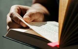 De hand van een jonge man slaat een bladzijde uit de BIjbel om.