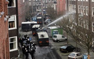Een politievoertuig spuit water op een hoog pand.